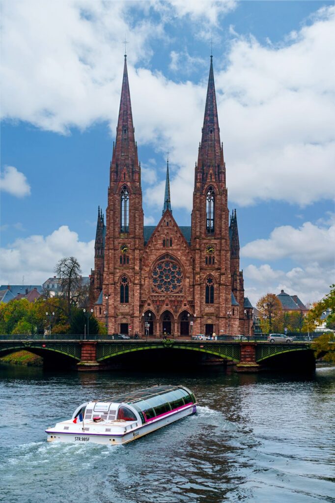 A stunning Gothic church along a tranquil riverside in Strasbourg, France, showcasing historic architecture and serene travel aesthetics.