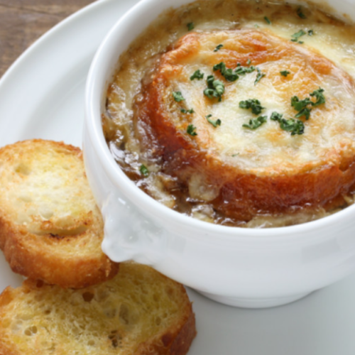 A warm, comforting bowl of French onion soup topped with melted Gruyère cheese, a crispy slice of toasted baguette, and garnished with fresh thyme, served in an oven-safe crock.