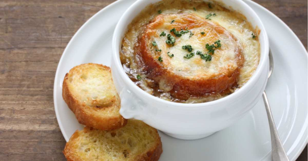 A warm, comforting bowl of French onion soup topped with melted Gruyère cheese, a crispy slice of toasted baguette, and garnished with fresh thyme, served in an oven-safe crock.