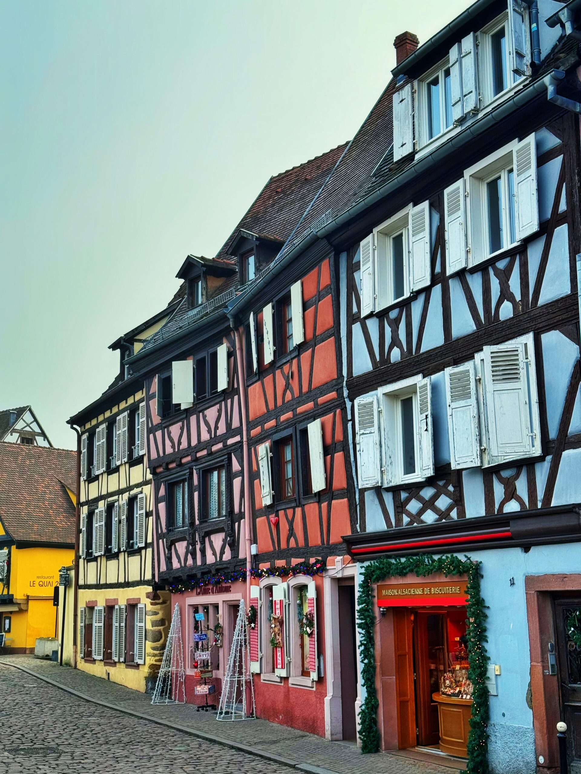 Vibrant row of colorful half-timbered houses in Colmar, showcasing the town's charming Alsatian architecture, set along cobblestone streets with flower-filled window boxes.